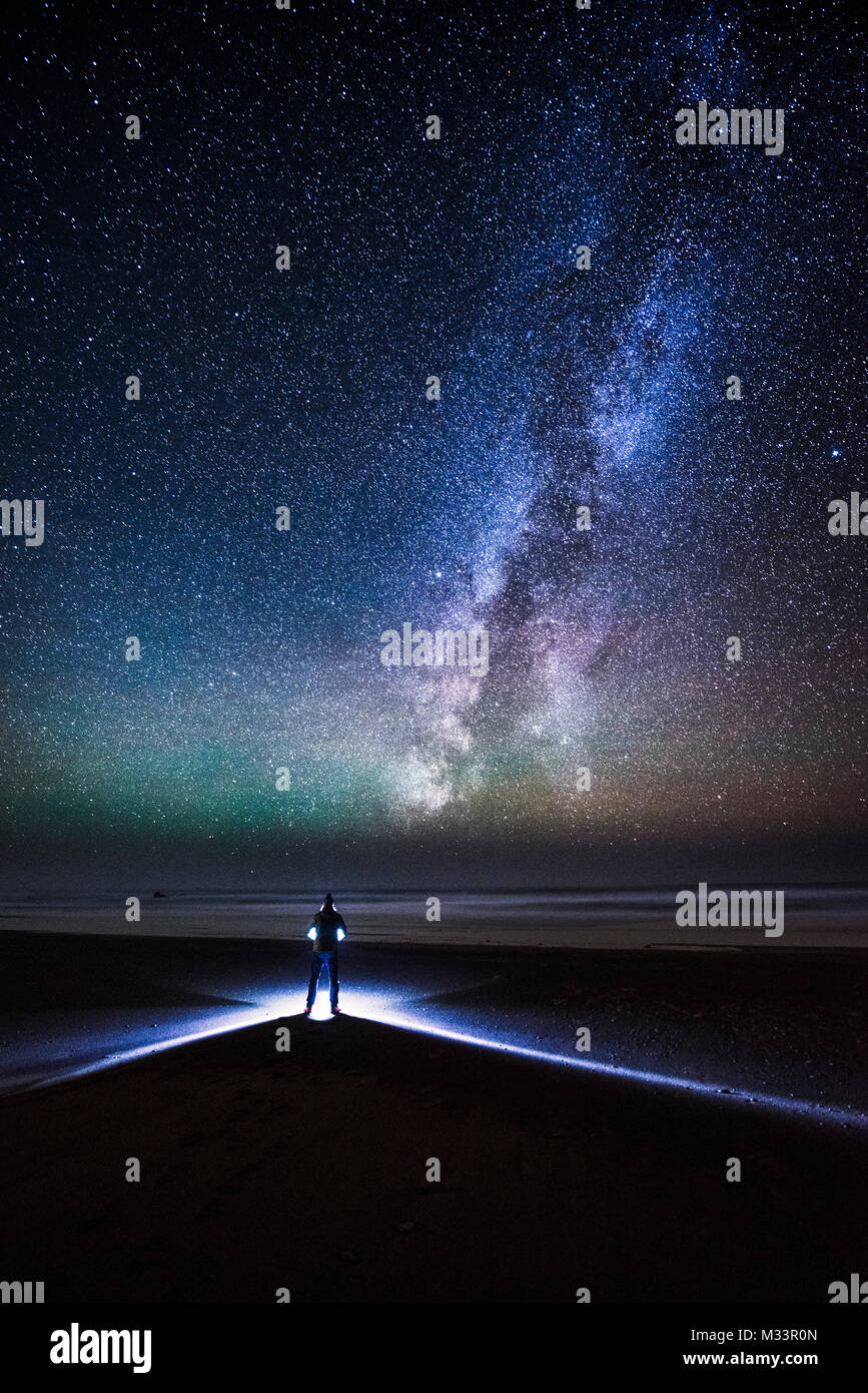 A man stands on Westport Beach on a perfectly clear night looking out over the Pacific Ocean, the Milky Way and stars above. Stock Photo