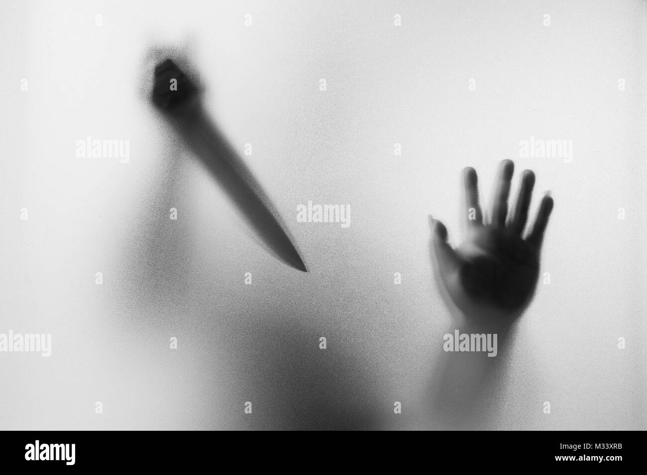 Horror Murderer. Dangerous man behind the frosted glass with a knife on his hand.Halloween background.Black and white picture Stock Photo