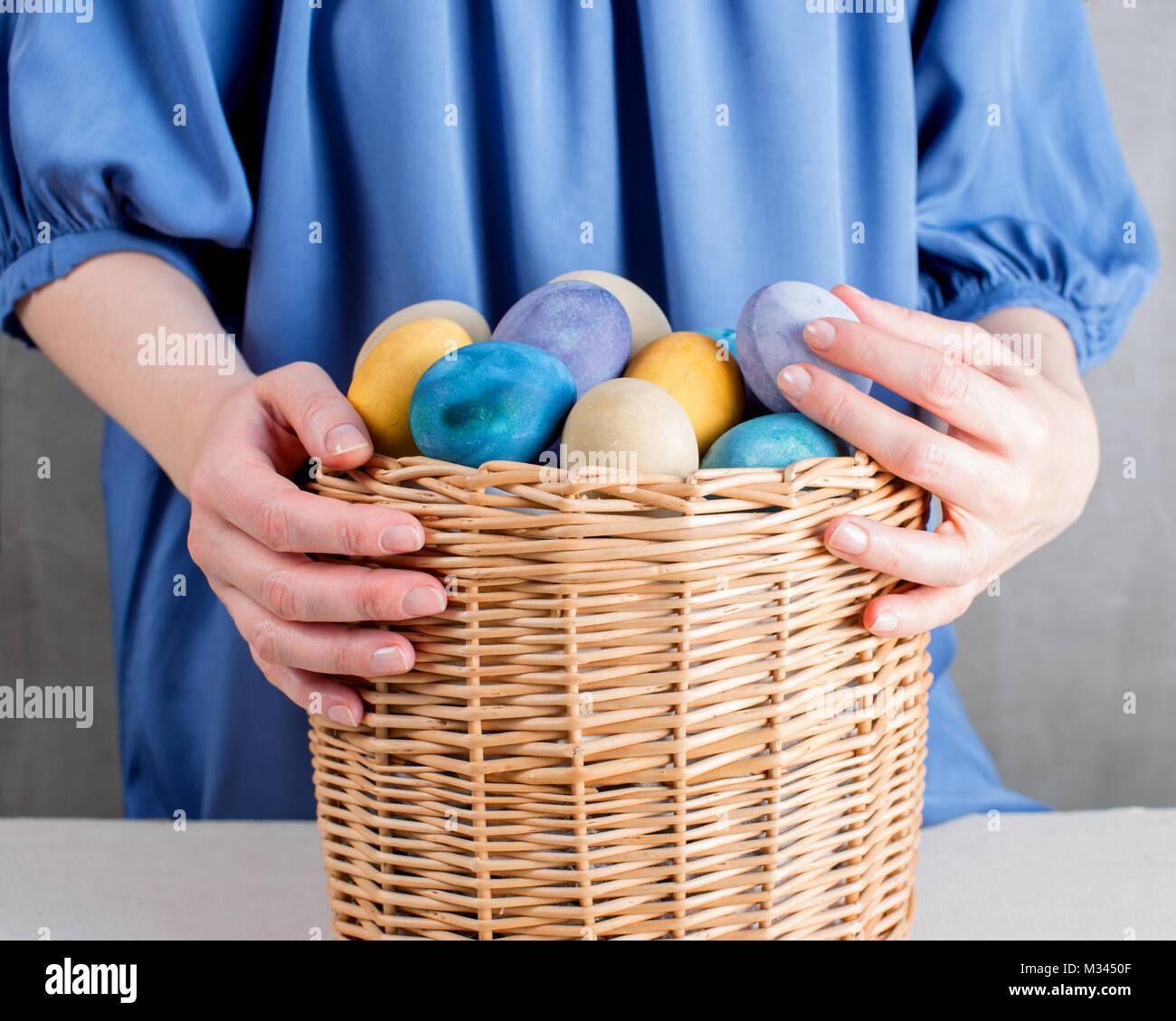 Woman in the blue dress holding the basket with colored yellow easter eggs Stock Photo
