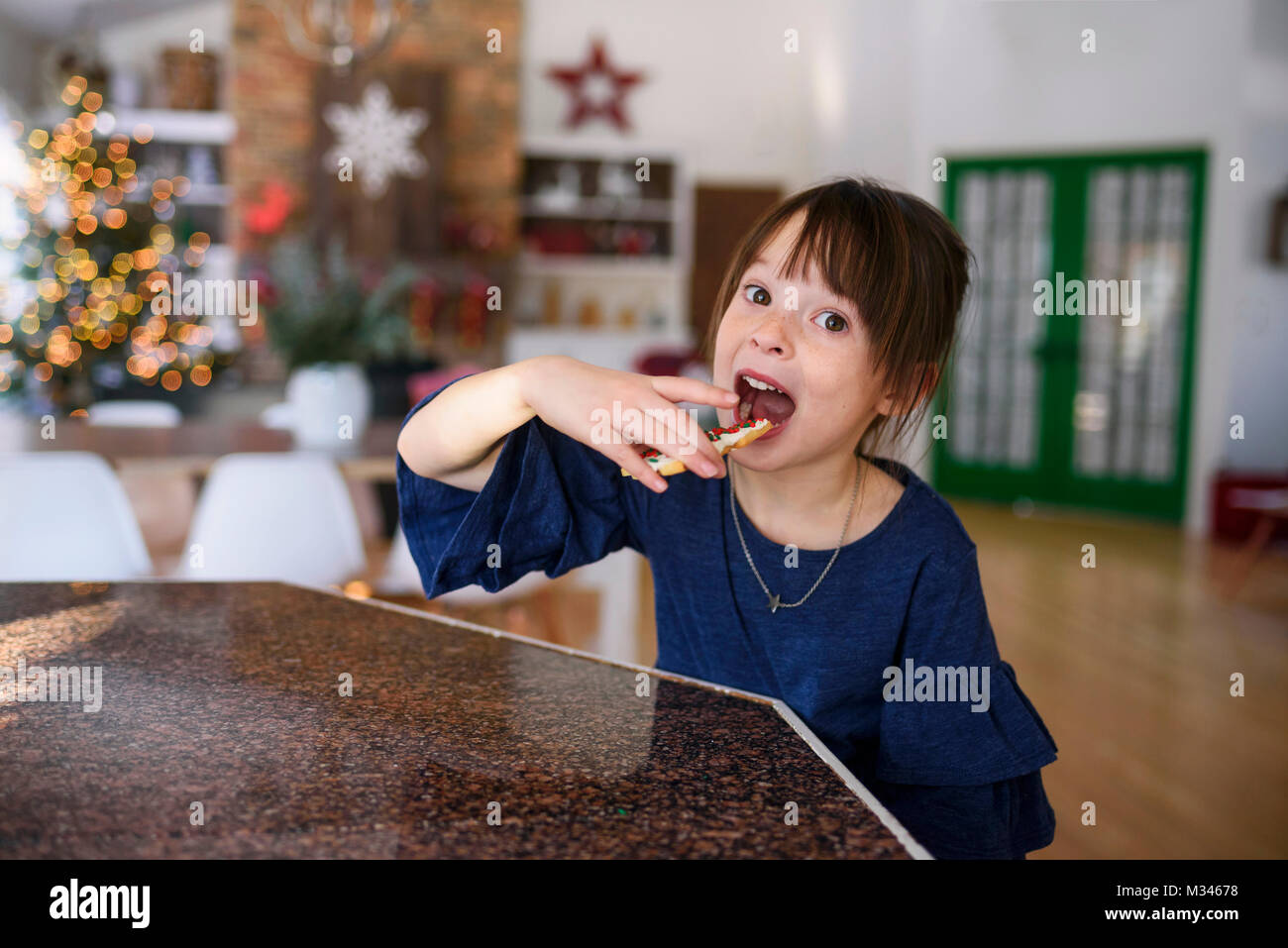 Girl standing in a kitchen eating a Christmas cookie Stock Photo
