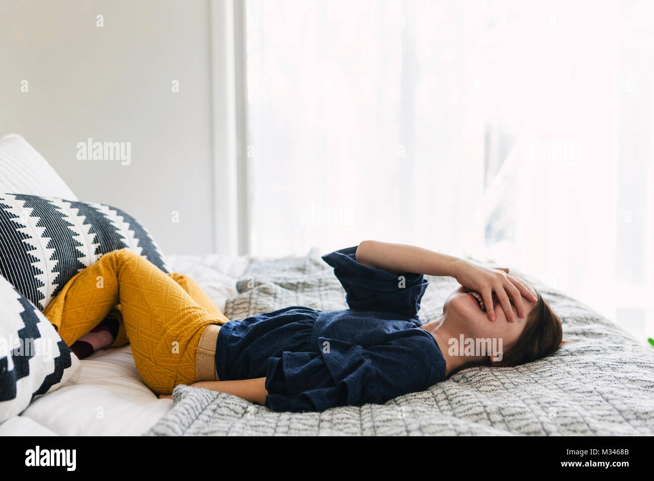 Girl lying on her bed laughing with her hand covering her eyes Stock Photo