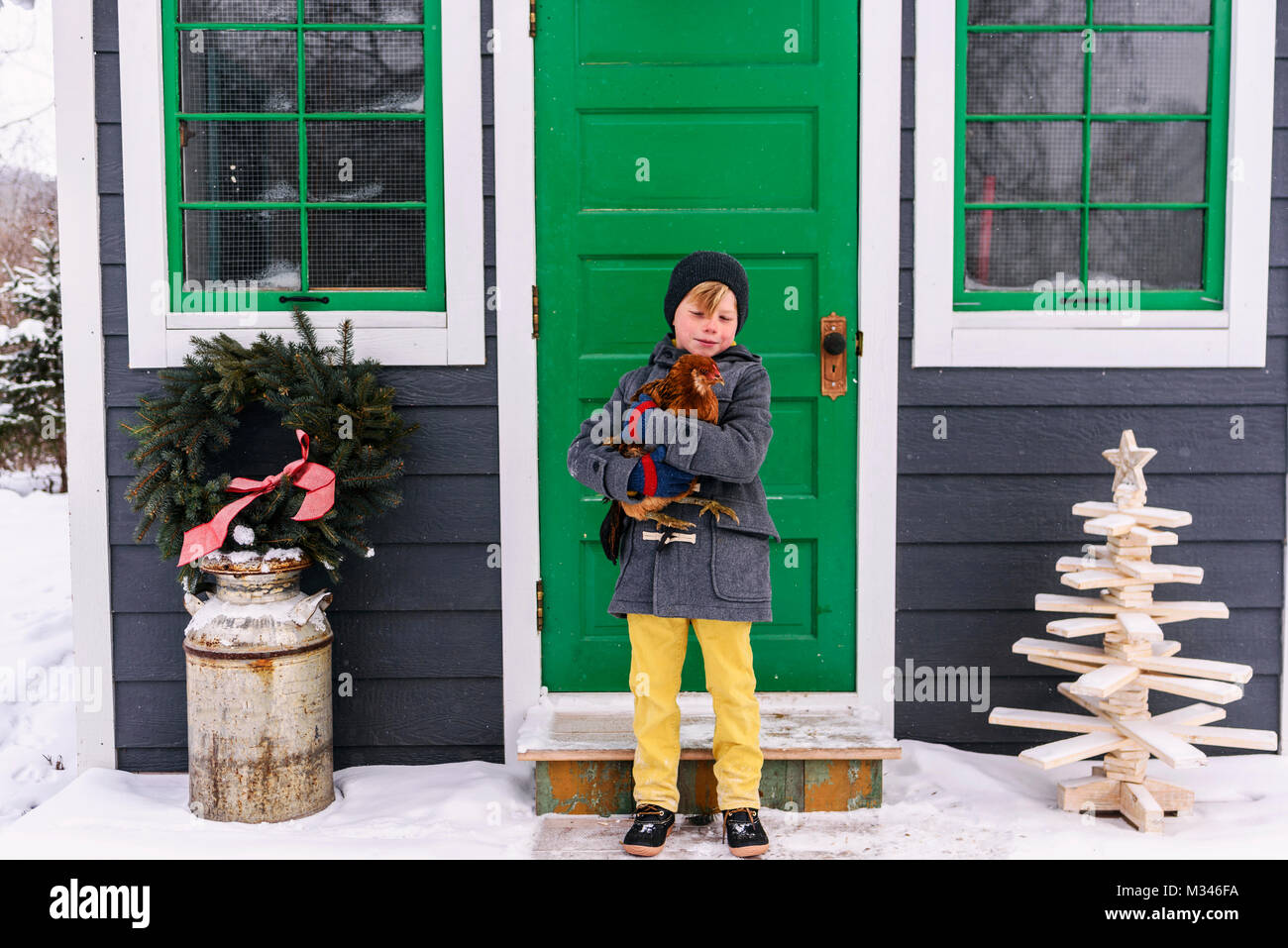 Boy standing outside a house holding a chicken Stock Photo