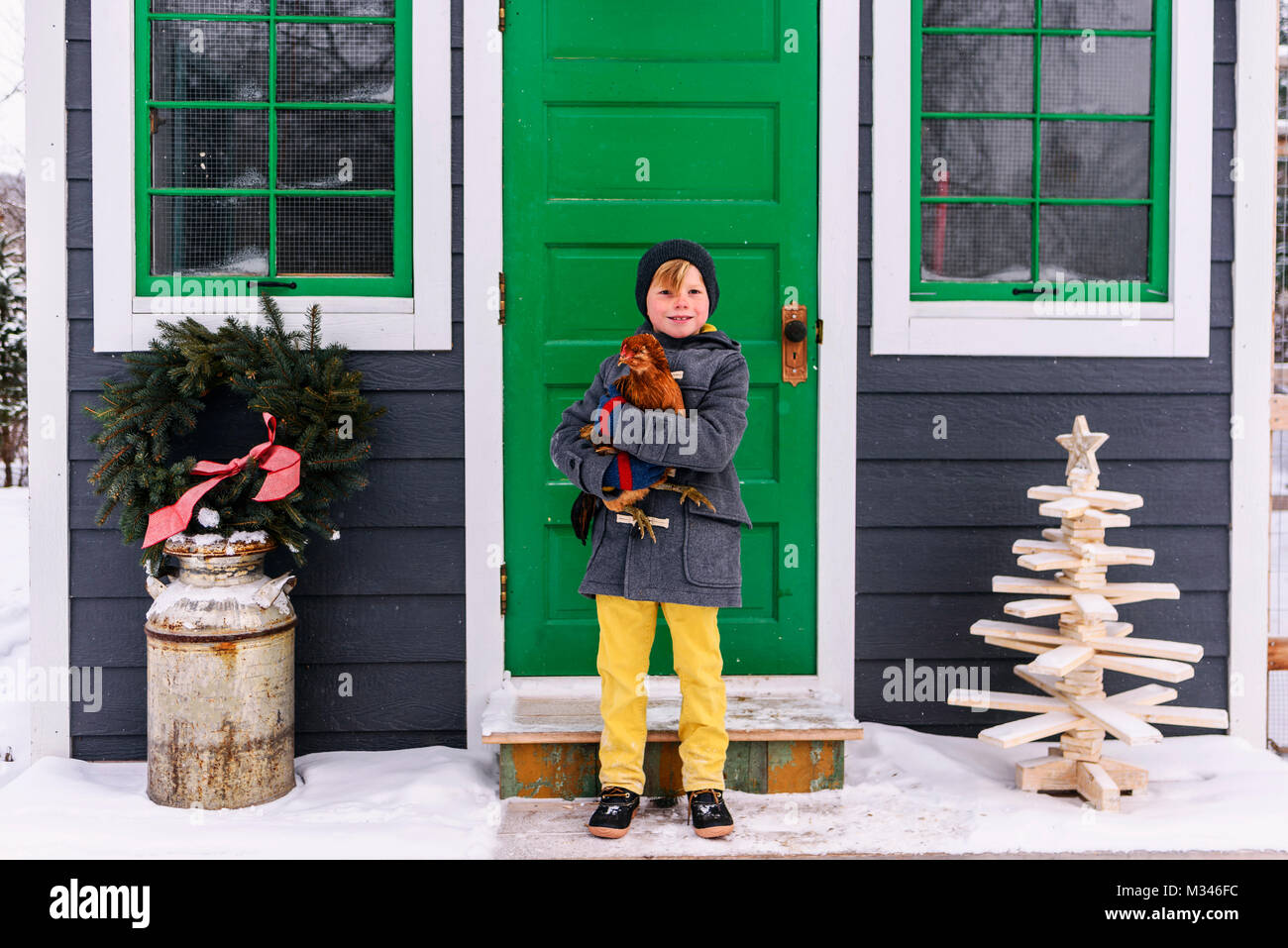 Boy standing outside a house holding a chicken Stock Photo