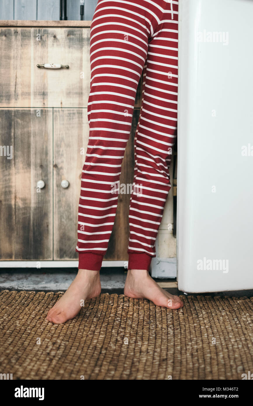Woman's legs standing by a fridge in the kitchen Stock Photo