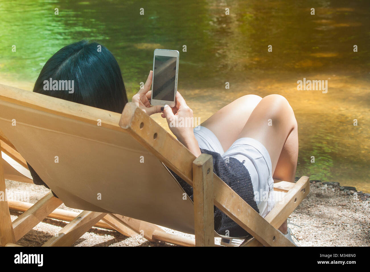 Relaxation Concept : Woman sitting on wooden bench beside the river and holding hers smartphone. Stock Photo