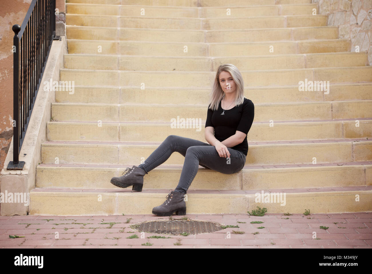Beautiful blonde girl in jeans and t-shirt sitting on steps Stock Photo