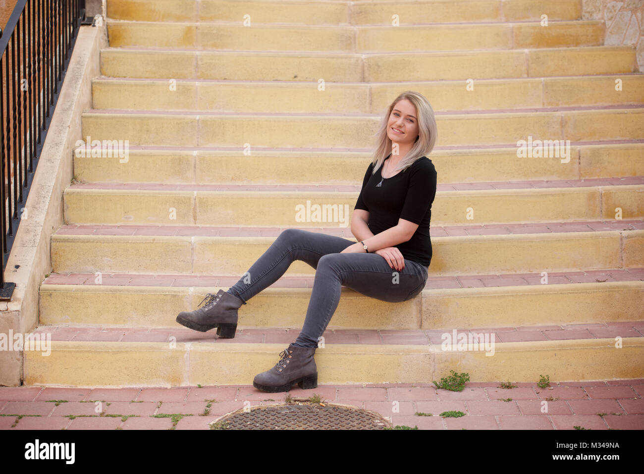 Beautiful blonde girl in jeans and t-shirt sitting on steps Stock Photo