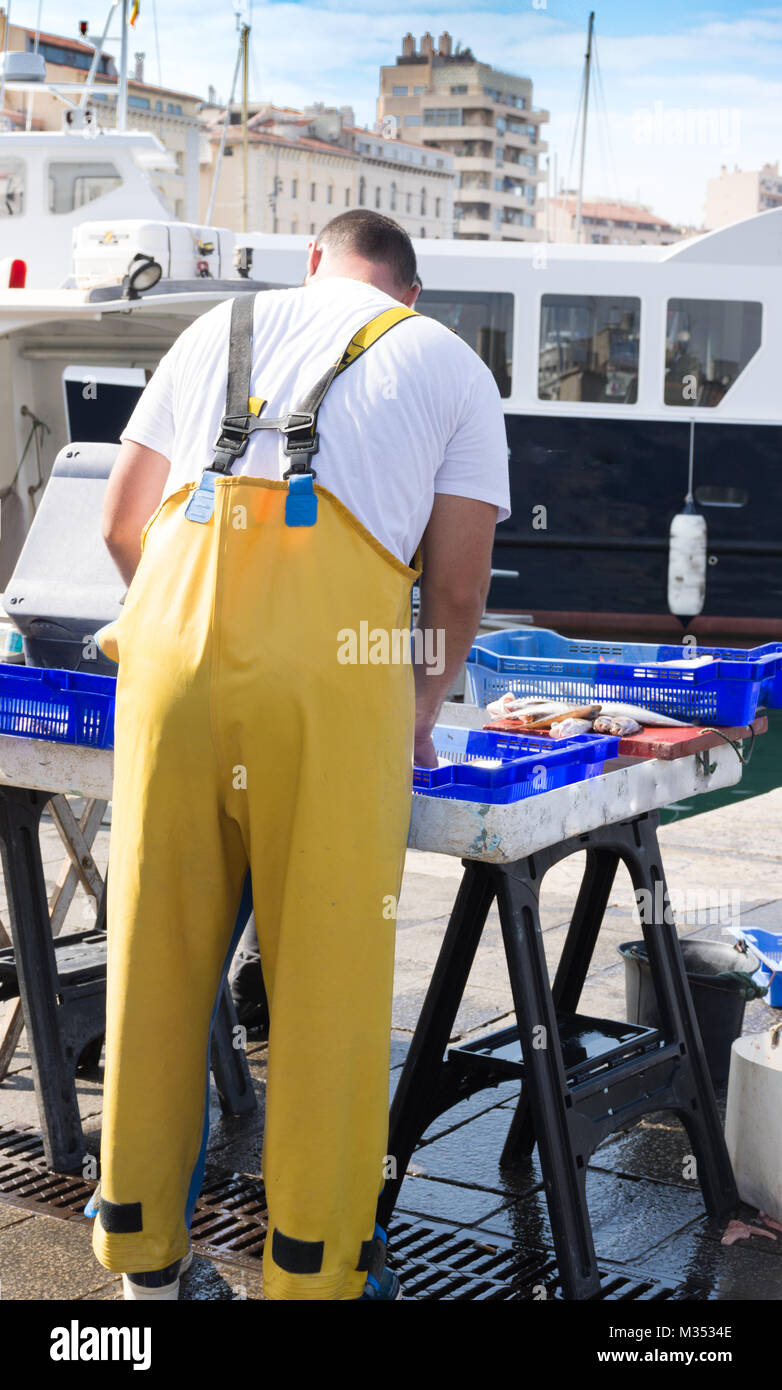 The back of a fisherman in yellow waterproof overalls arranging