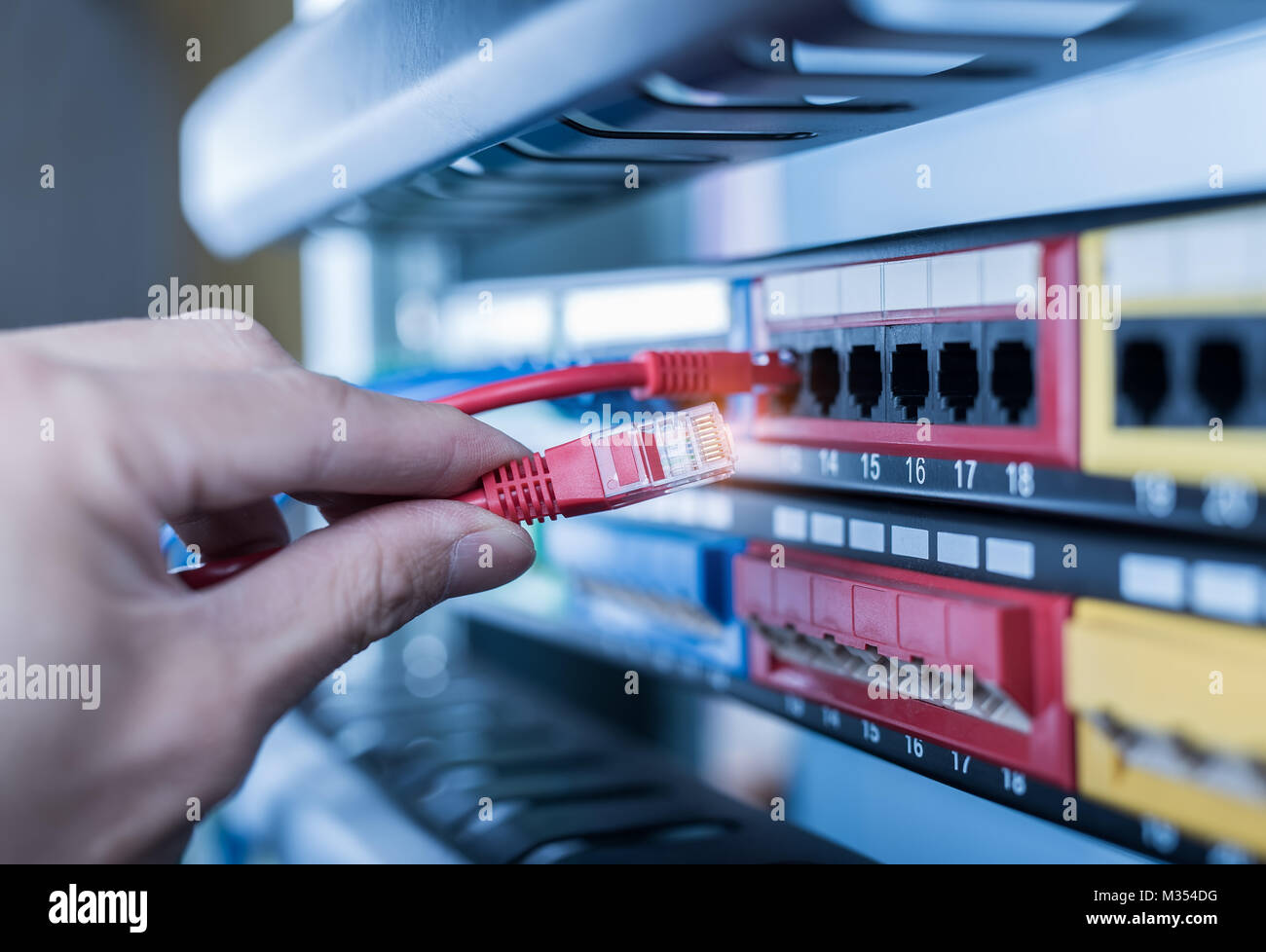 administrator holding network cables connected to servers Stock Photo