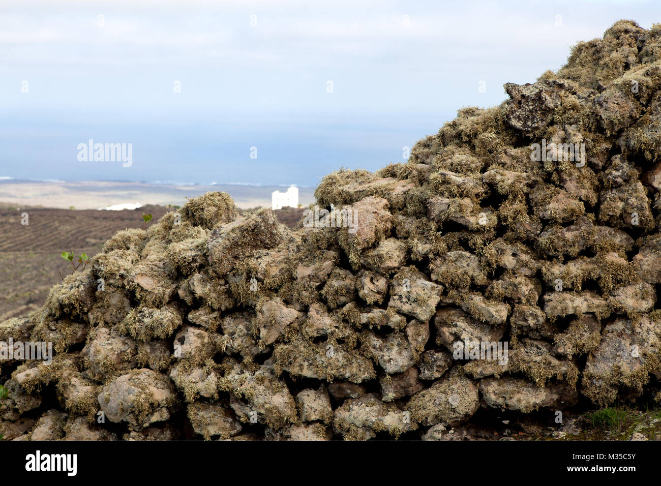 Yé, Haría, Lanzarote, Spain: An old wall made of volcanic stone and covered with lichen, with a view of the countryside from the Volcan of la Corona. Stock Photo