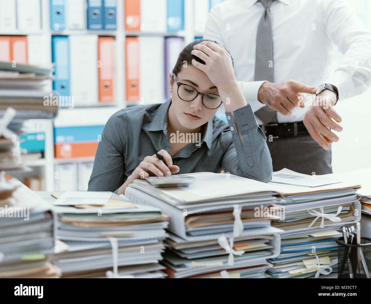 Demanding boss pointing to his watch and asking to his employee to hurry up, his secretary is frustrated and overwhelmed by work: business and deadlin Stock Photo