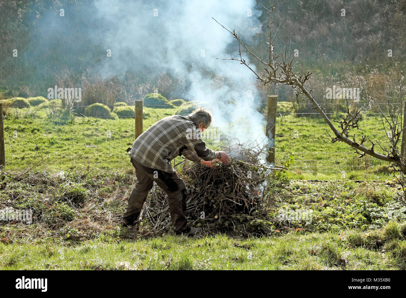 A man lighting making a bonfire in the garden tidying up and burning old sticks and branches garden waste in winter February Wales UK  KATHY DEWITT Stock Photo