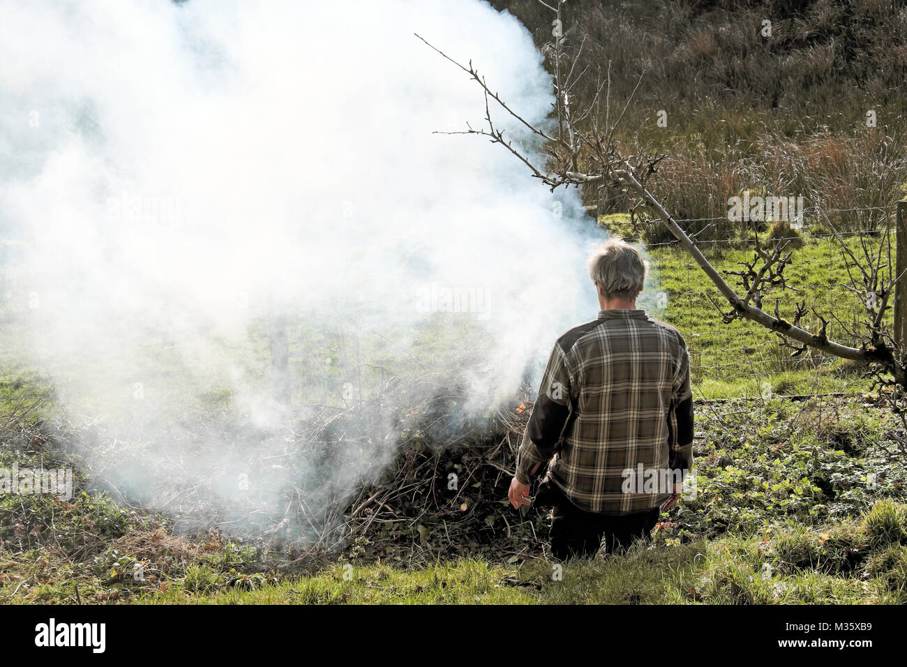 A man lighting a bonfire in the garden tidying up and burning old sticks and branches in preparation for spring February in Wales UK  KATHY DEWITT Stock Photo