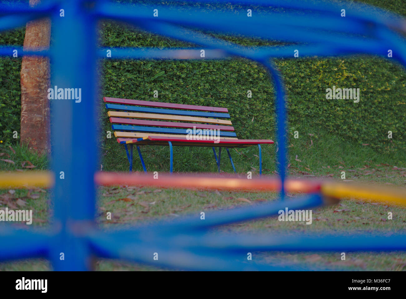 A colorful park bench shoot through a blue roundabout at a playground. Stock Photo