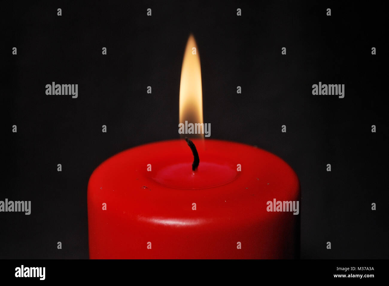 A red candle is burning in the darkness Stock Photo