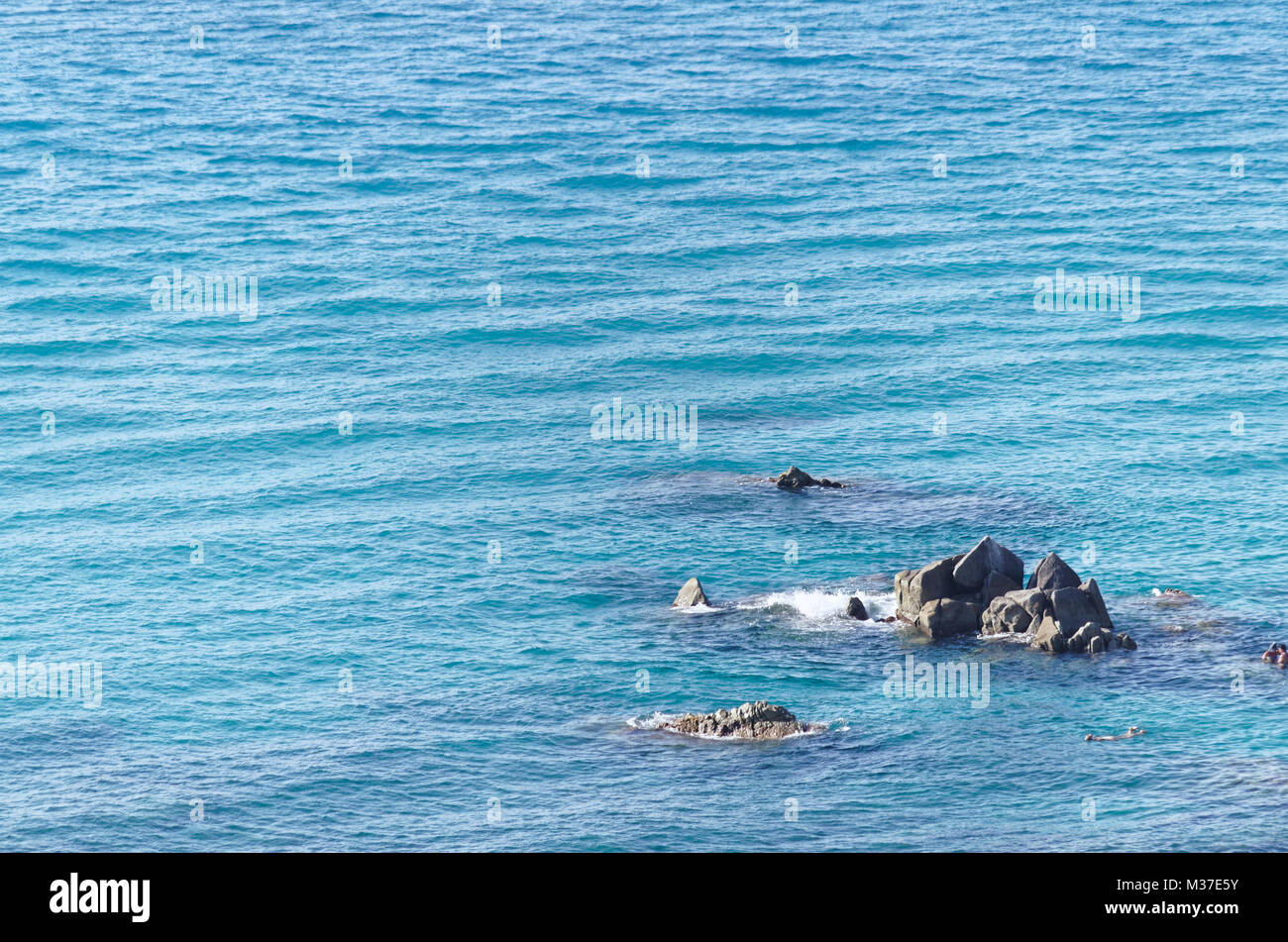 Pointed rocks in the blue water of tyrrhenian sea, near beach in tropea Stock Photo