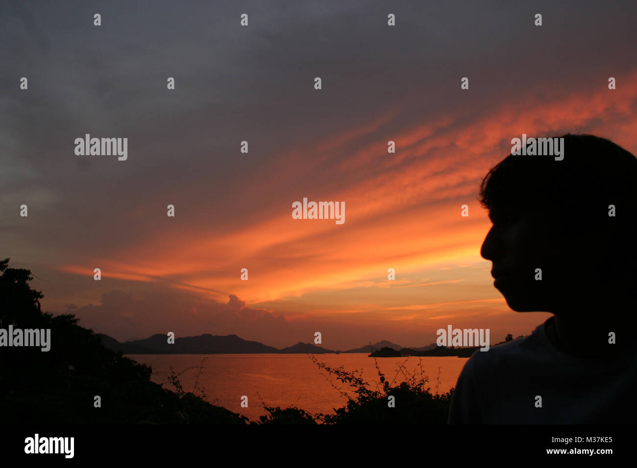 A tourist watches a spectacular sunset over the Batang Ai National Park reservoir, in Sarawak, Borneo,  August 3, 2005 Stock Photo