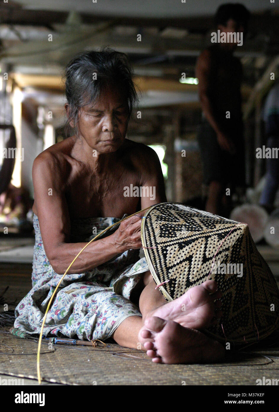 A local resident weaves a hat in a longhouse set in rainforest in the Batang Ai National Park, in Sarawak, Malaysia August 3, 2005. Stock Photo