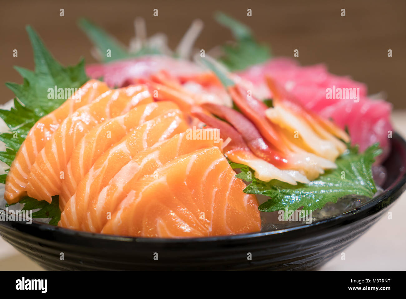 Mixed sliced fish sashimi on ice in black bowl. Sashimi Salmon Tuna Hamachi Prawn and Surf Calm set, raw fish, japanese food in Asian restuarant. Stock Photo