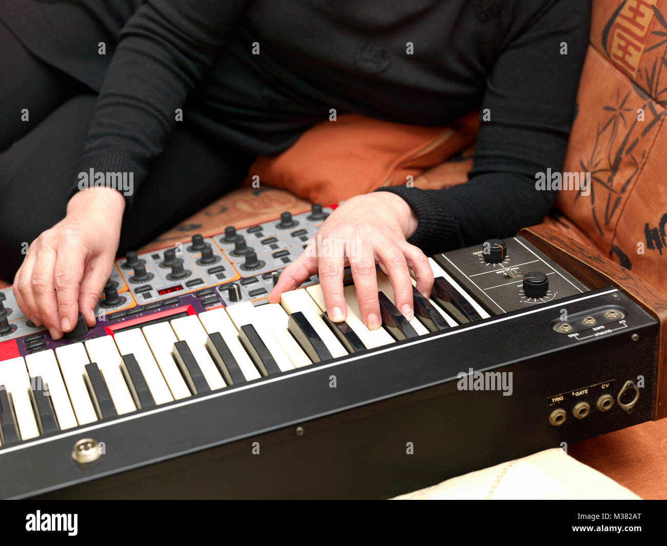 Woman lying on a sofa and playing synthesizers, indoor closeup Stock Photo