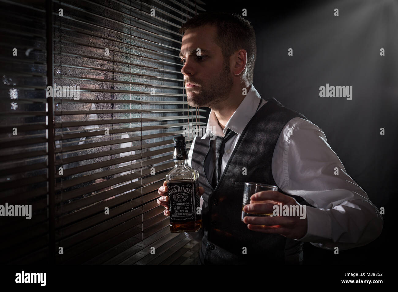 Gangster holding a bottle of whisky and glass while looking out the