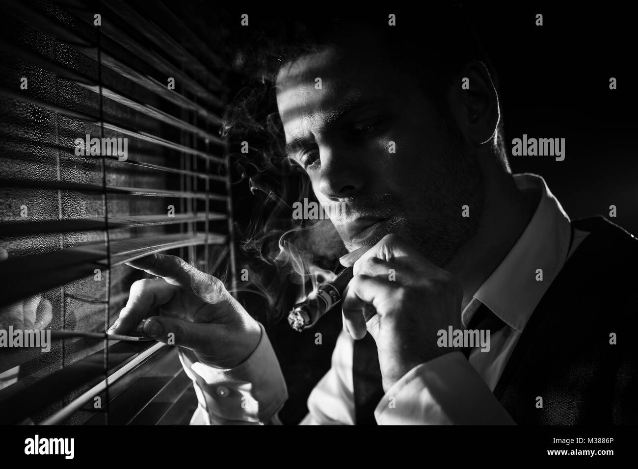 Gangster smoking a cigar while looking out the window at a car headlights Stock Photo