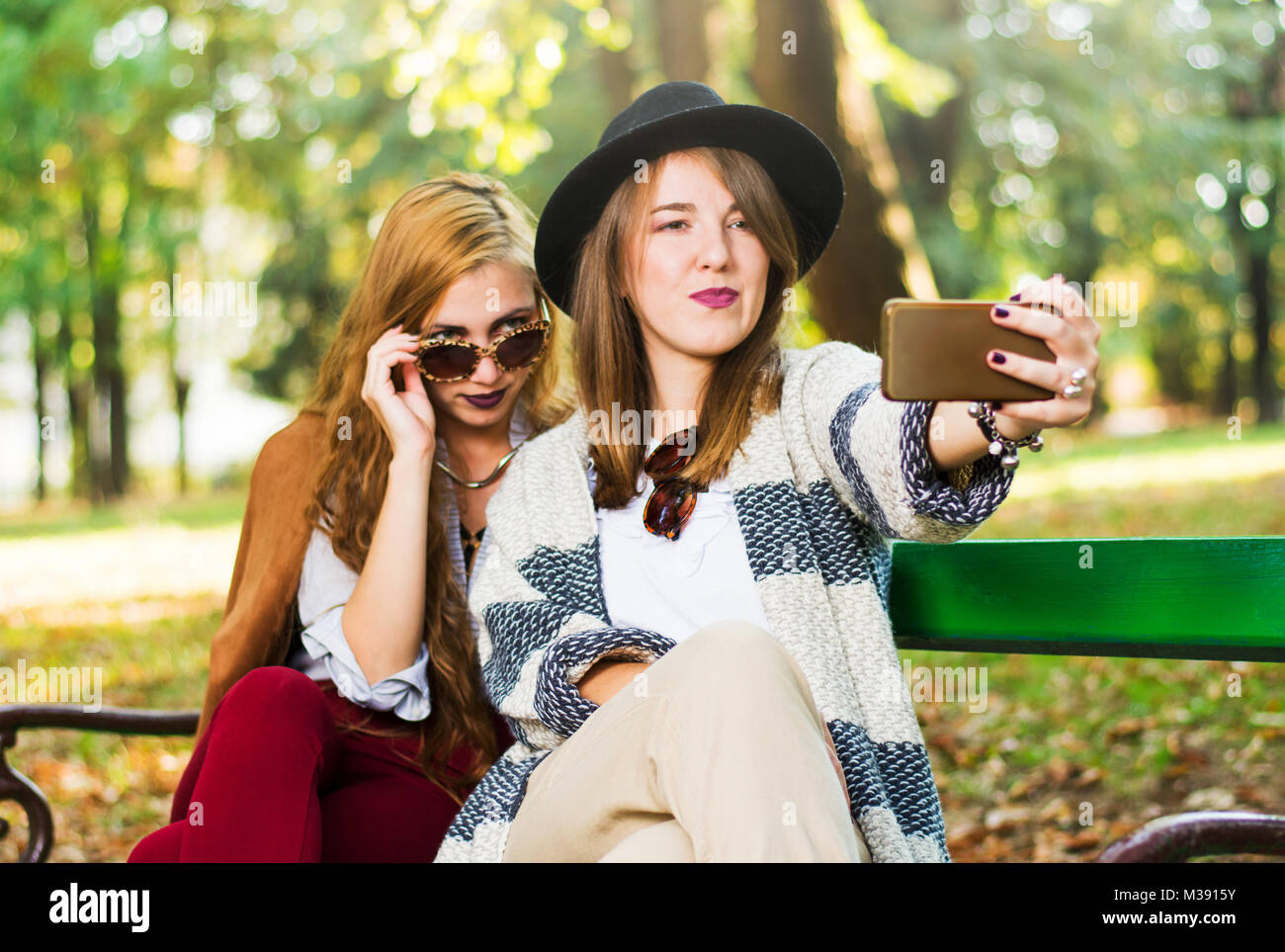 Girlfriends taking a selfie on a bench in the park Stock Photo