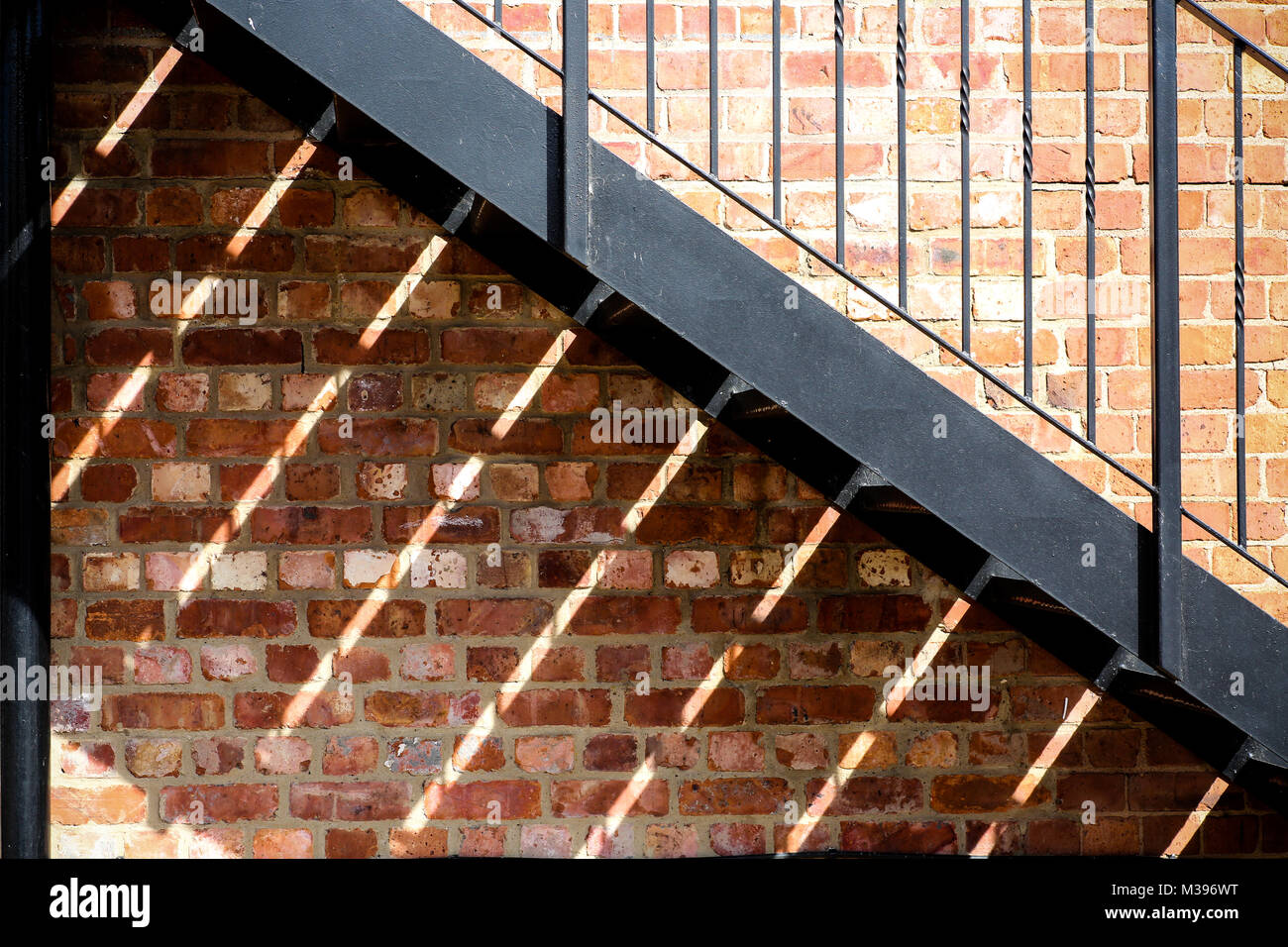 A fire escape cast geometric shadows onto a red brick wall Stock Photo