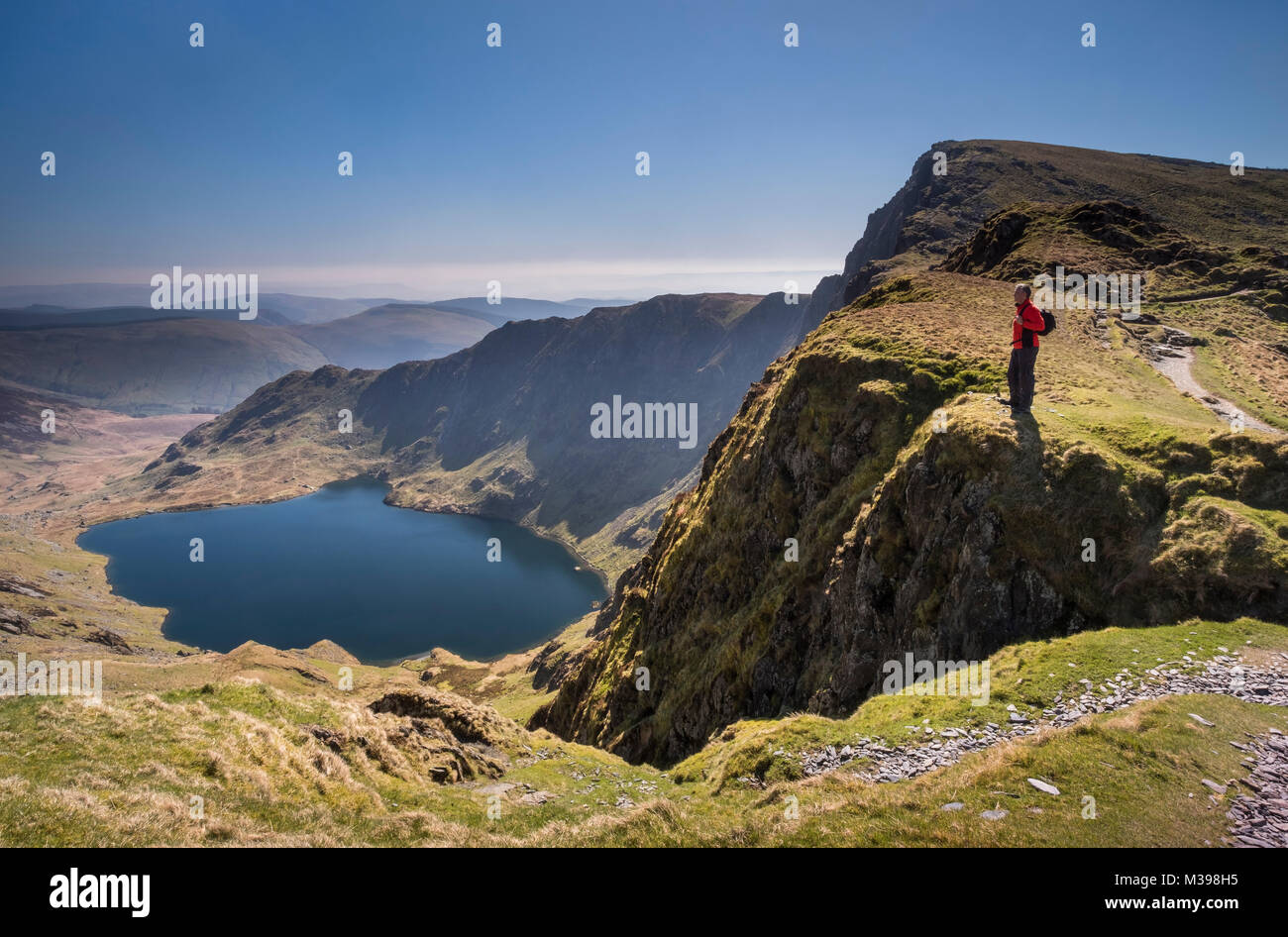 Walker looking out over Llyn Cau from Craig Cau, Cadair Idris, Snowdonia National Park, North Wales, UK MODEL RELEASED Stock Photo