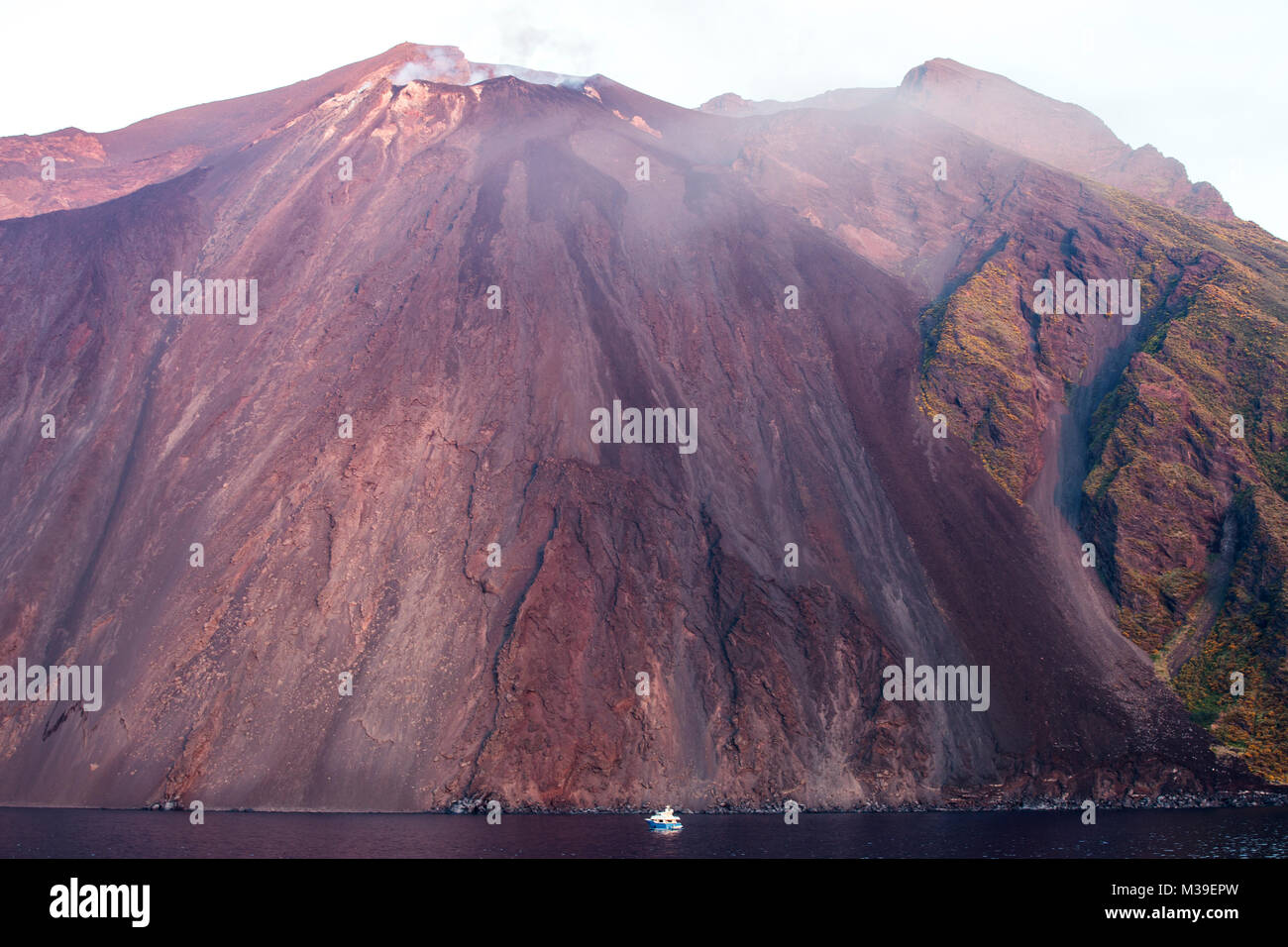 Stromboli volcano with a few faint puffs from the crater.  A sense of scale is given by the small boat in the foreground. Stock Photo