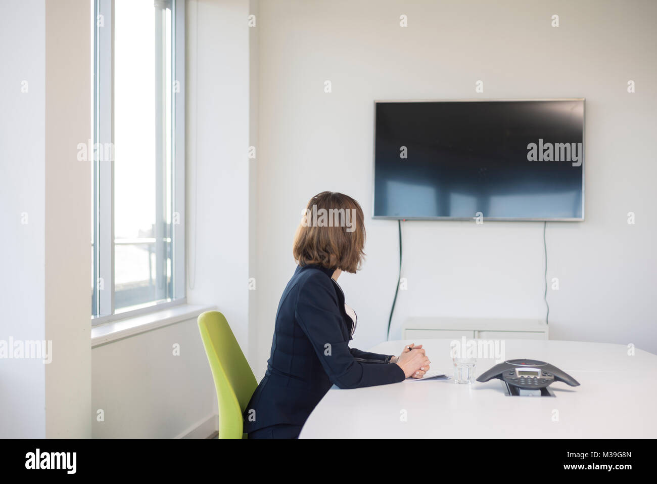 White smart consultant worker business woman sits in a meeting room looking at the video conference computer screen on the wall while in a video chat Stock Photo