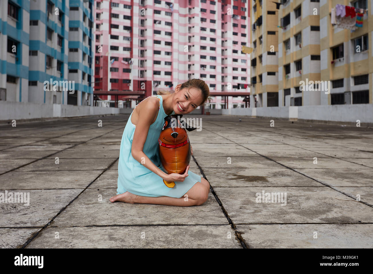 Happy fun-loving young female dancer with toy balloon dog at Rochor Center, Singapore.  These colourful buildings are historical landmark. Stock Photo
