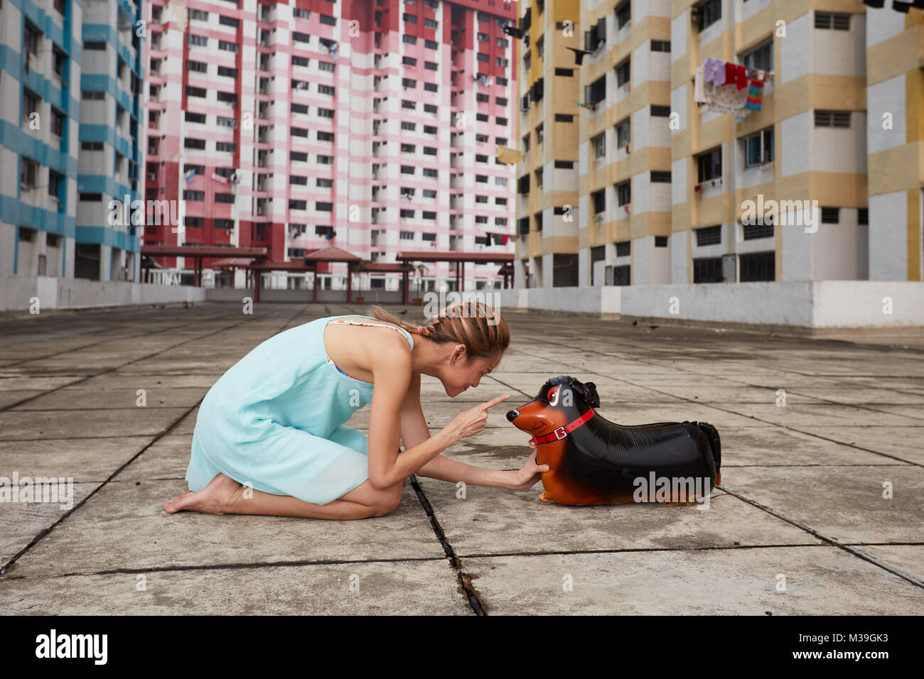 Happy fun-loving young female dancer with toy balloon dog at Rochor Center, Singapore.  These colourful buildings are historical landmark. Stock Photo