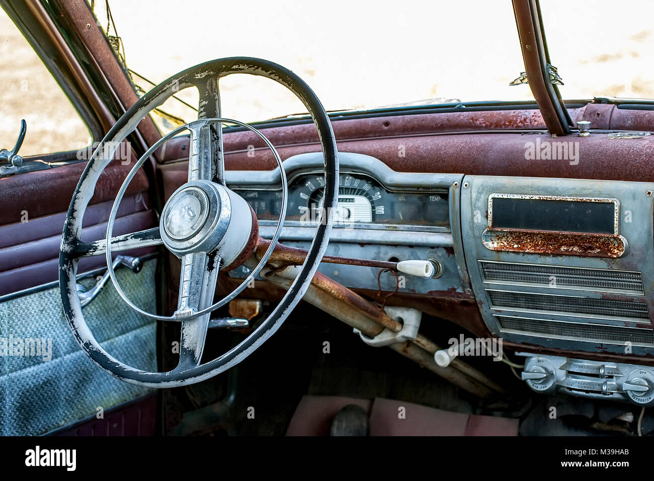 Interior of an old, rusted  and abandoned Plymouth automobile with old-fashioned steering wheel with sailboat logo. Stock Photo