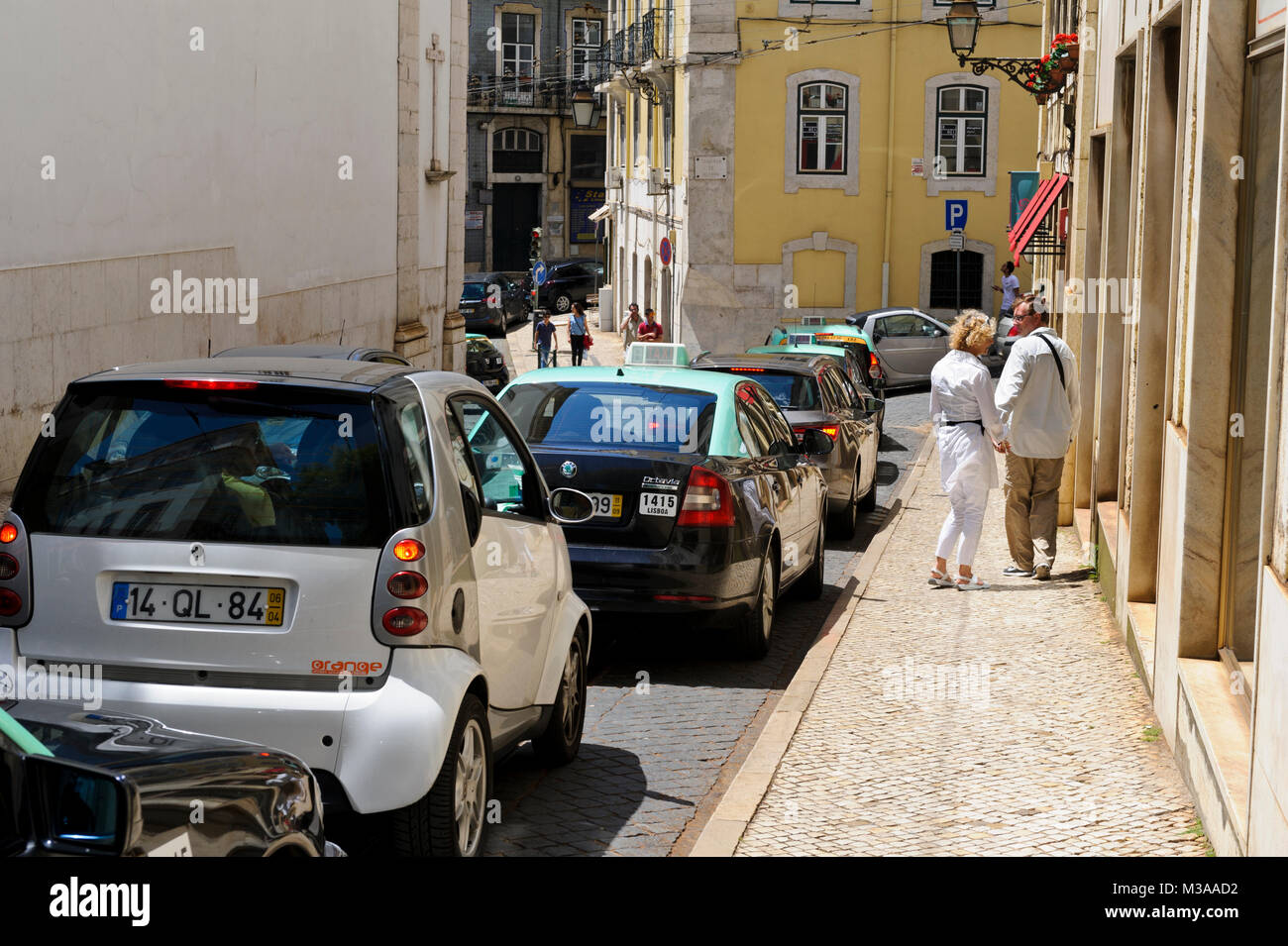 A couple walking on the pavement on the street while several cars passing by, Lisbon, Portugal Stock Photo