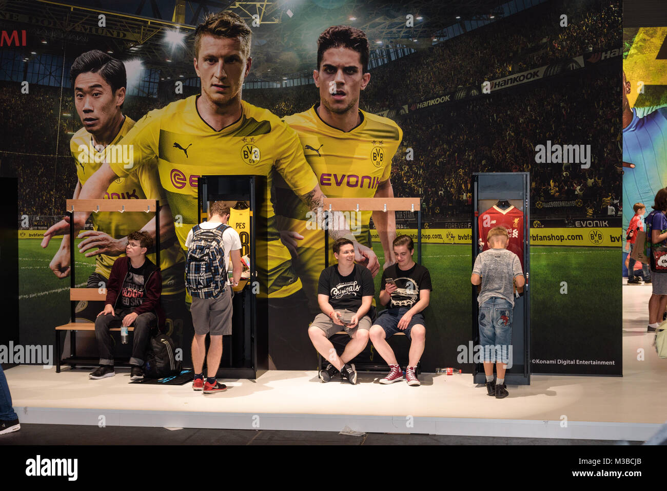 Cologne, Germany - August 24, 2017: Boys stand and sit in front of a BVB advertisement for Pro Evolution Soccer from the company Konami at Gamescome 2 Stock Photo
