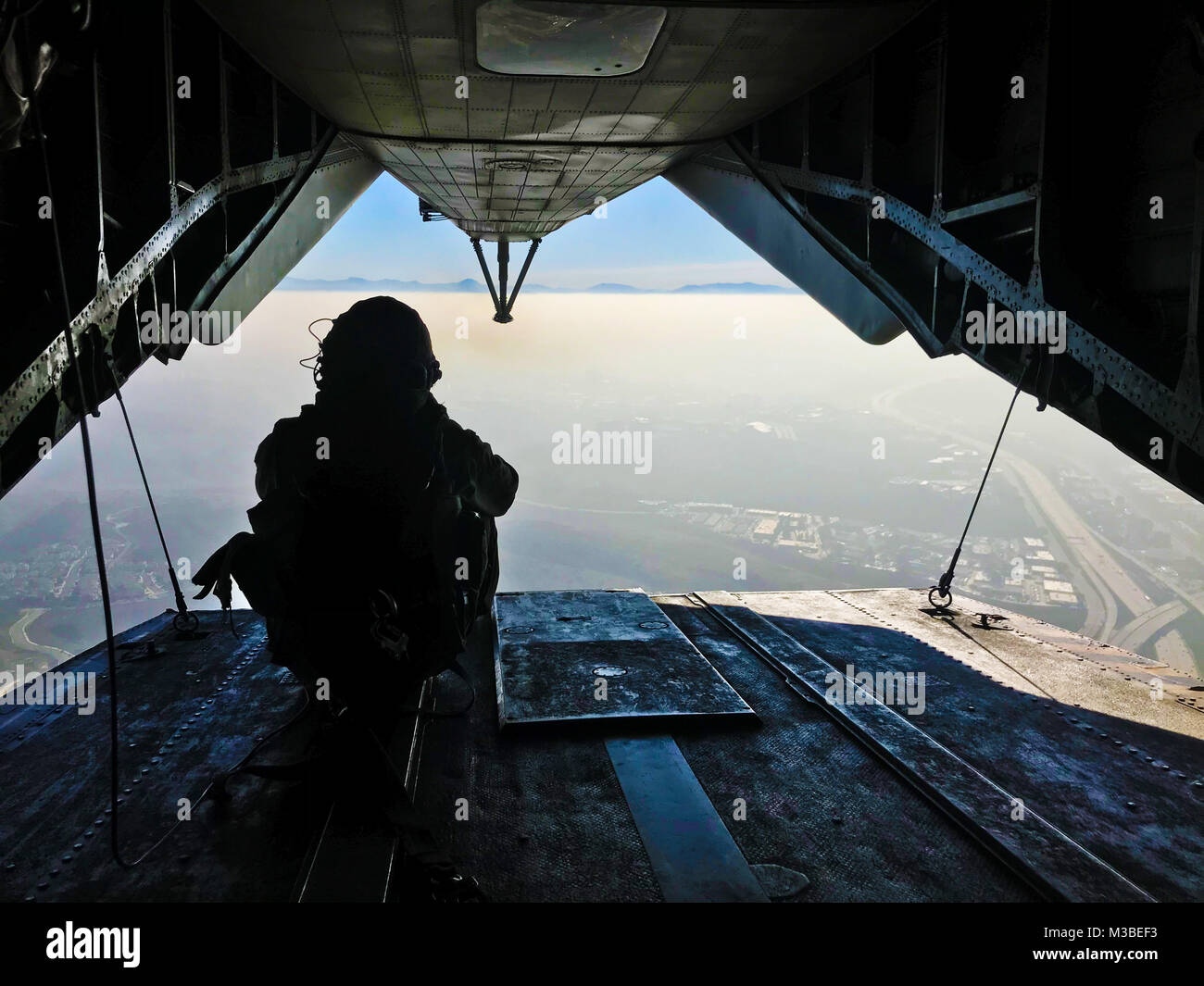 Sgt. Adam Collins, a CH-53E crew chief with Marine Heavy Helicopter Squadron (HMH) 465, scans the area below between jumps during flight and parachute operations with 1st Marine Reconnaissance Battalion at Marine Corps Base Camp Pendleton, Calif., Feb. 6. During parachute and flight operations, the ground combat element and the air combat element work together to ensure safety and mission accomplishment during training. (U.S. Marine Corps photo by Sgt. David Bickel/Released) Stock Photo