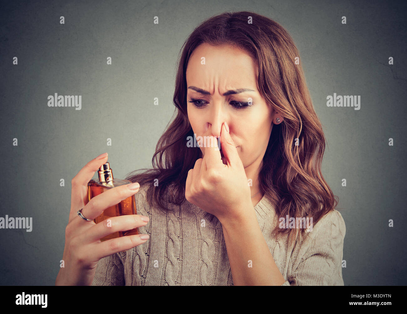 Young girl disgusted with unpleasant stinky perfume holding nose. Stock Photo