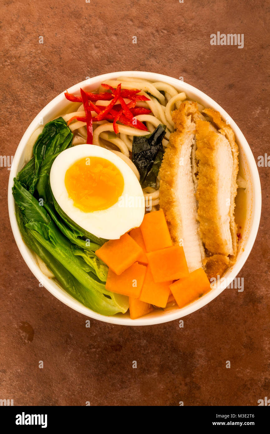 Japanese Style Panko Breadcrumbs Chicken And Noodle Broth or Soup With Sweet Potatoes Afainst A Red Tile Background Stock Photo