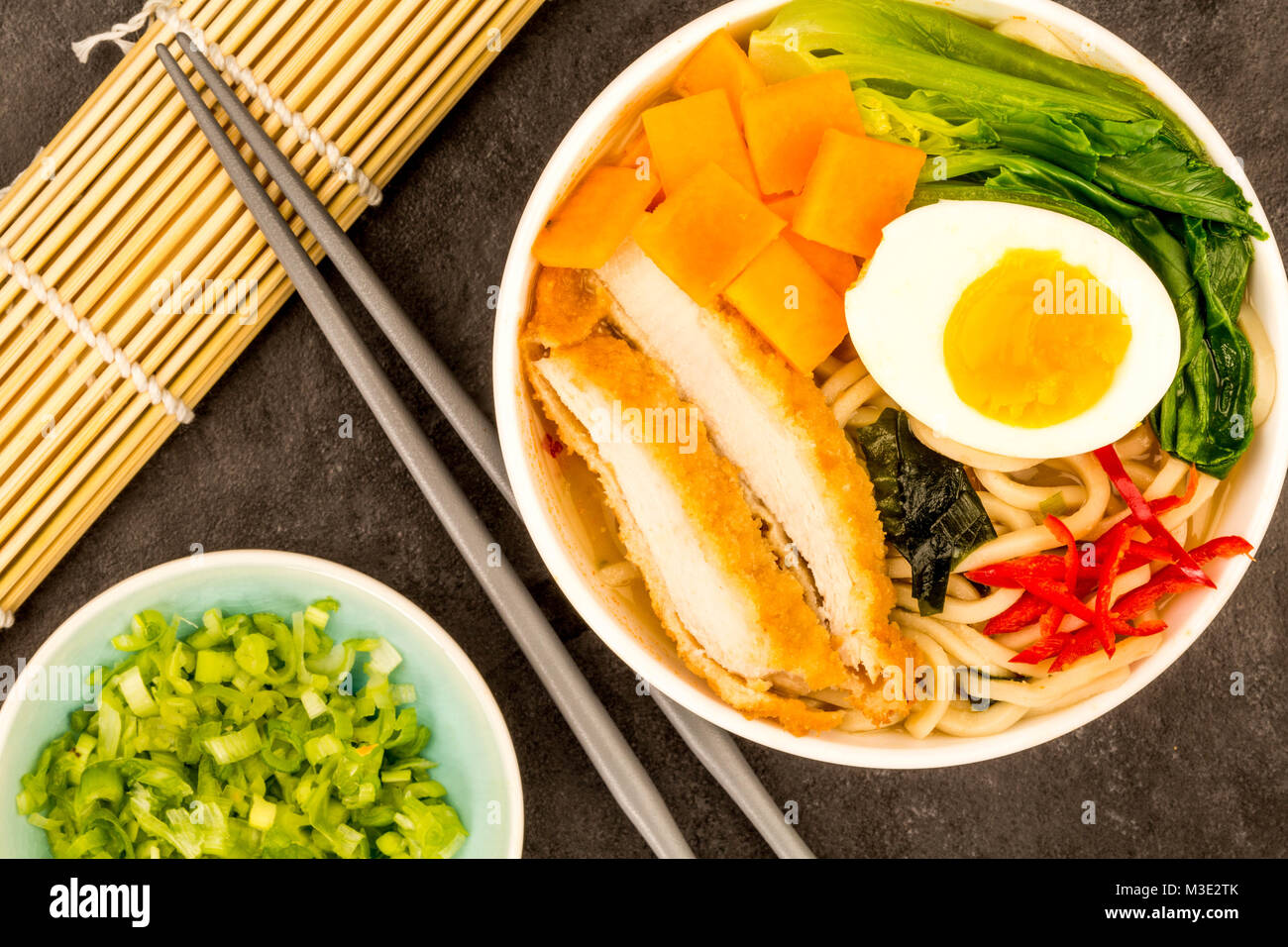 Japanese Style Panko Breadcrumbs Chicken And Noodle Broth or Soup With Sweet Potatoes Against A Black Tile Backgorund Stock Photo