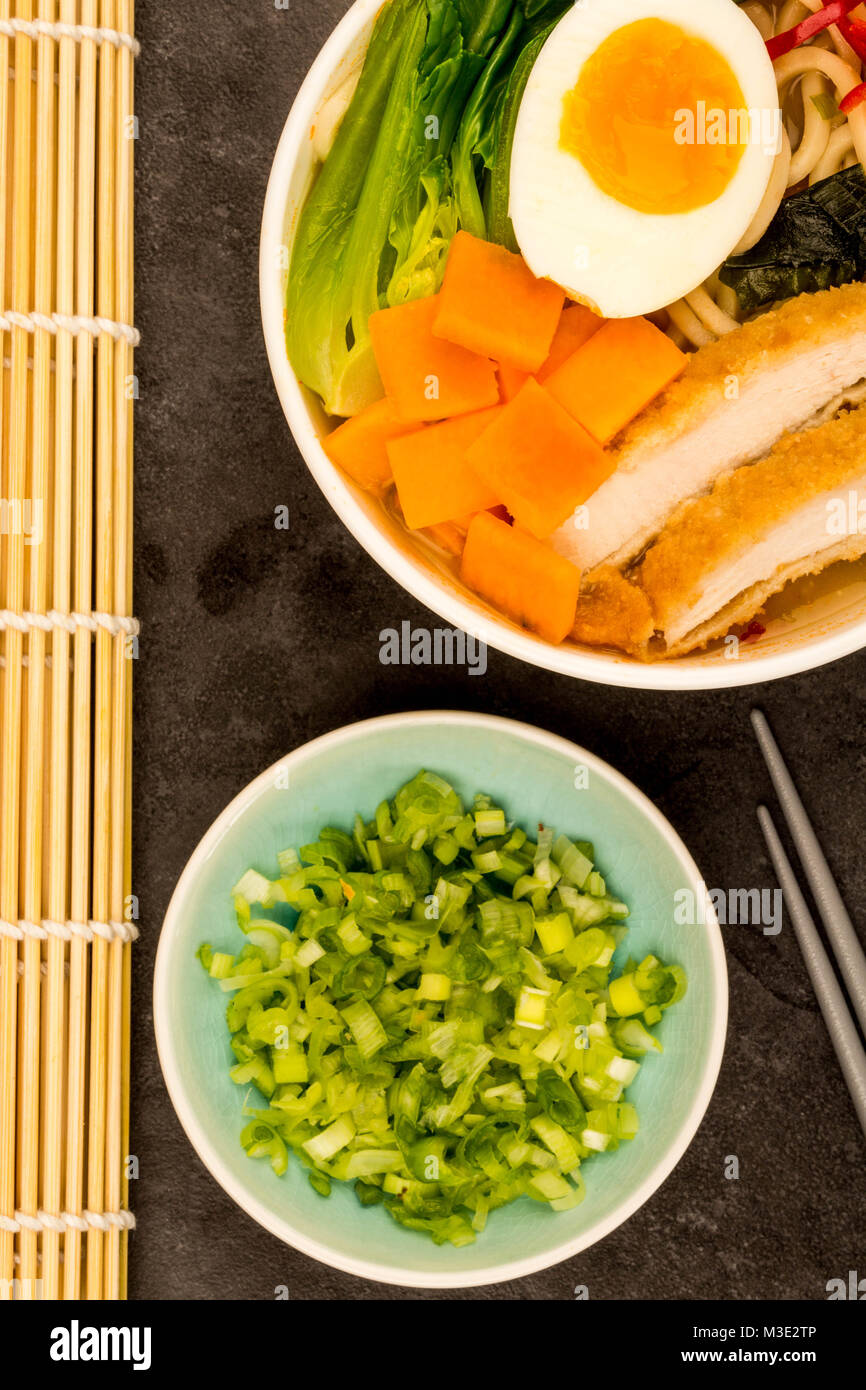 Japanese Style Panko Breadcrumbs Chicken And Noodle Broth or Soup With Sweet Potatoes Against A Black Tile Backgorund Stock Photo