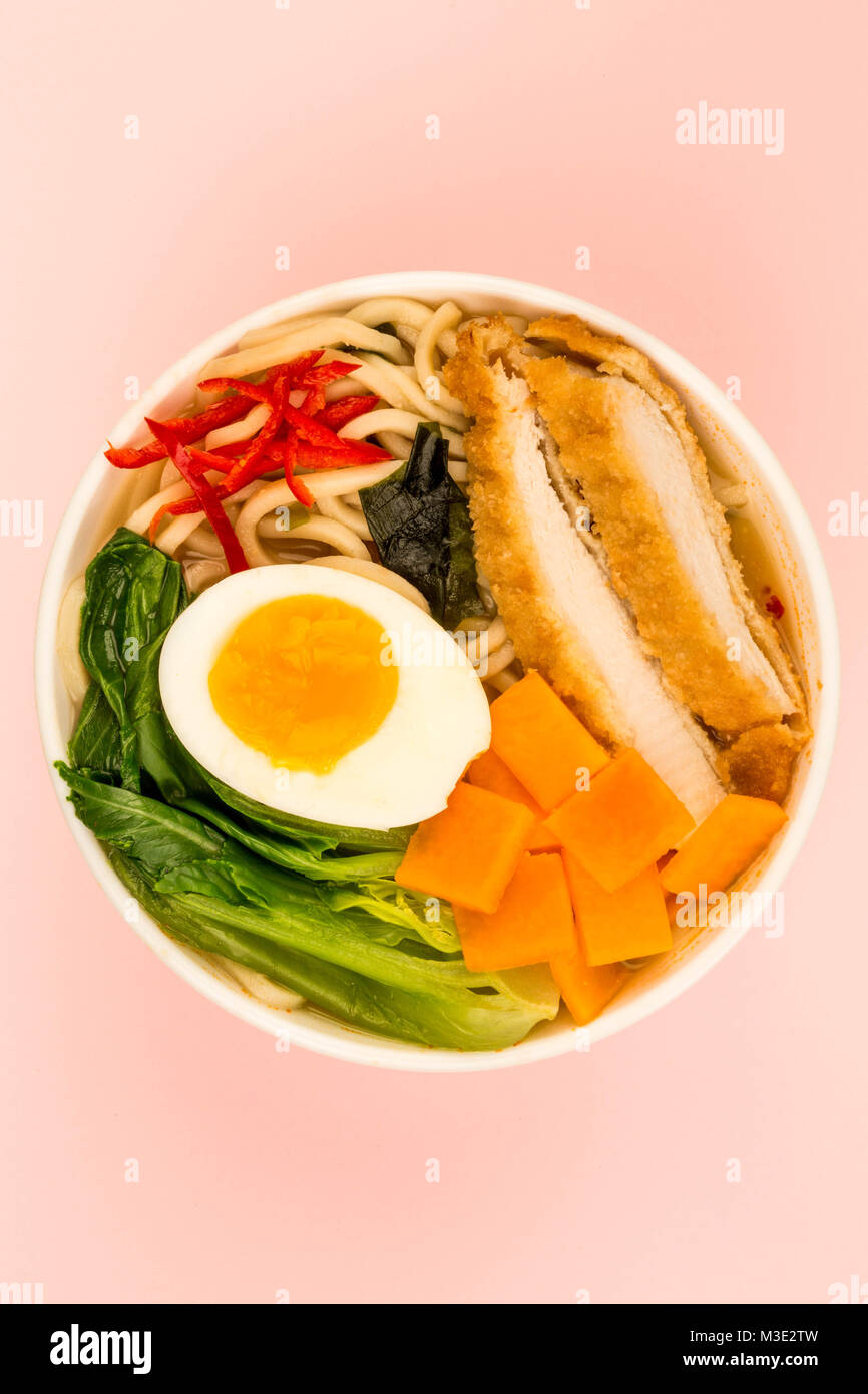 Japanese Style Panko Breadcrumbs Chicken And Noodle Broth or Soup With Sweet Potatoes Against A Pale Pink Background Stock Photo
