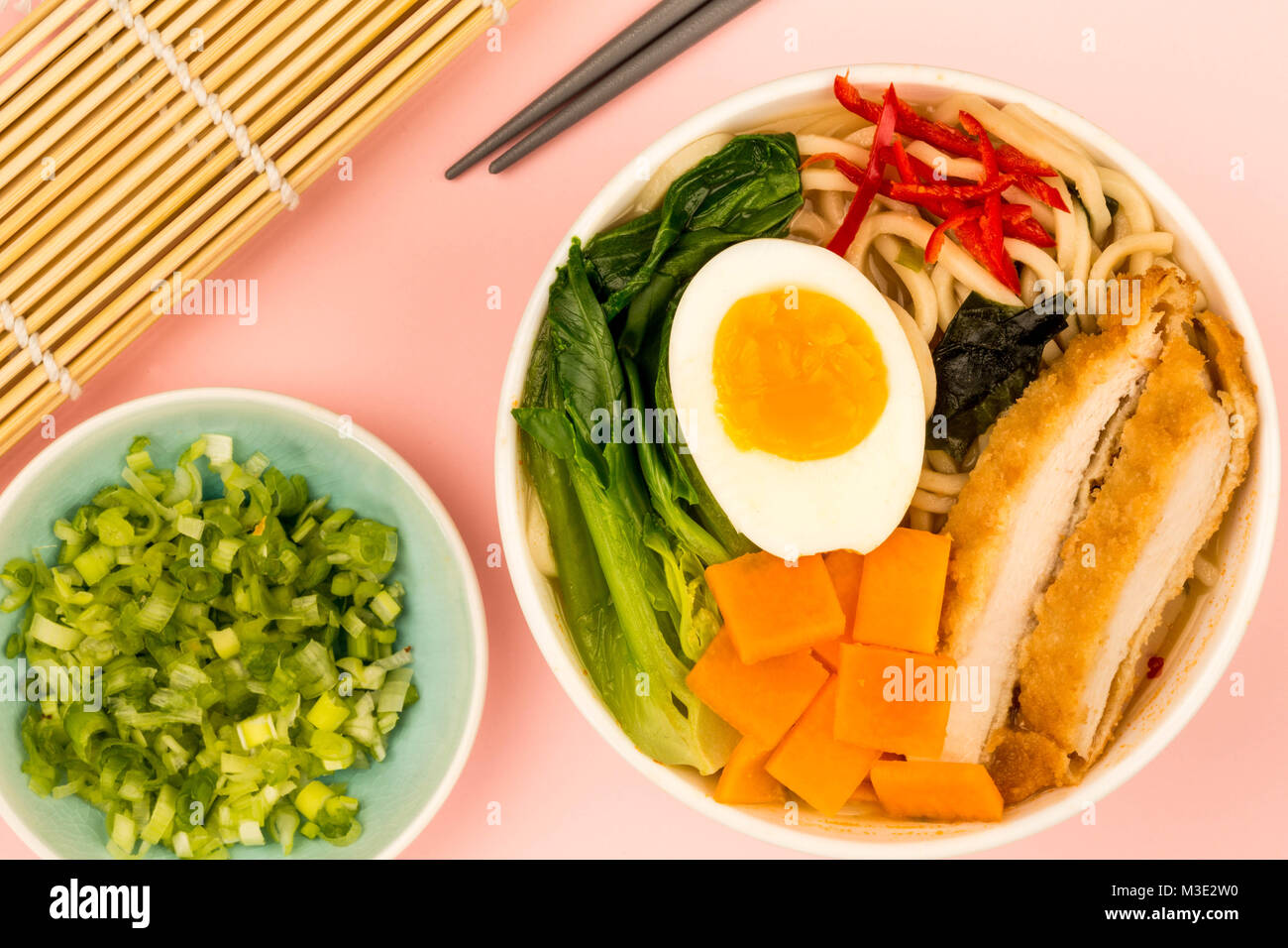 Japanese Style Panko Breadcrumbs Chicken And Noodle Broth or Soup With Sweet Potatoes Against A Pale Pink Background Stock Photo