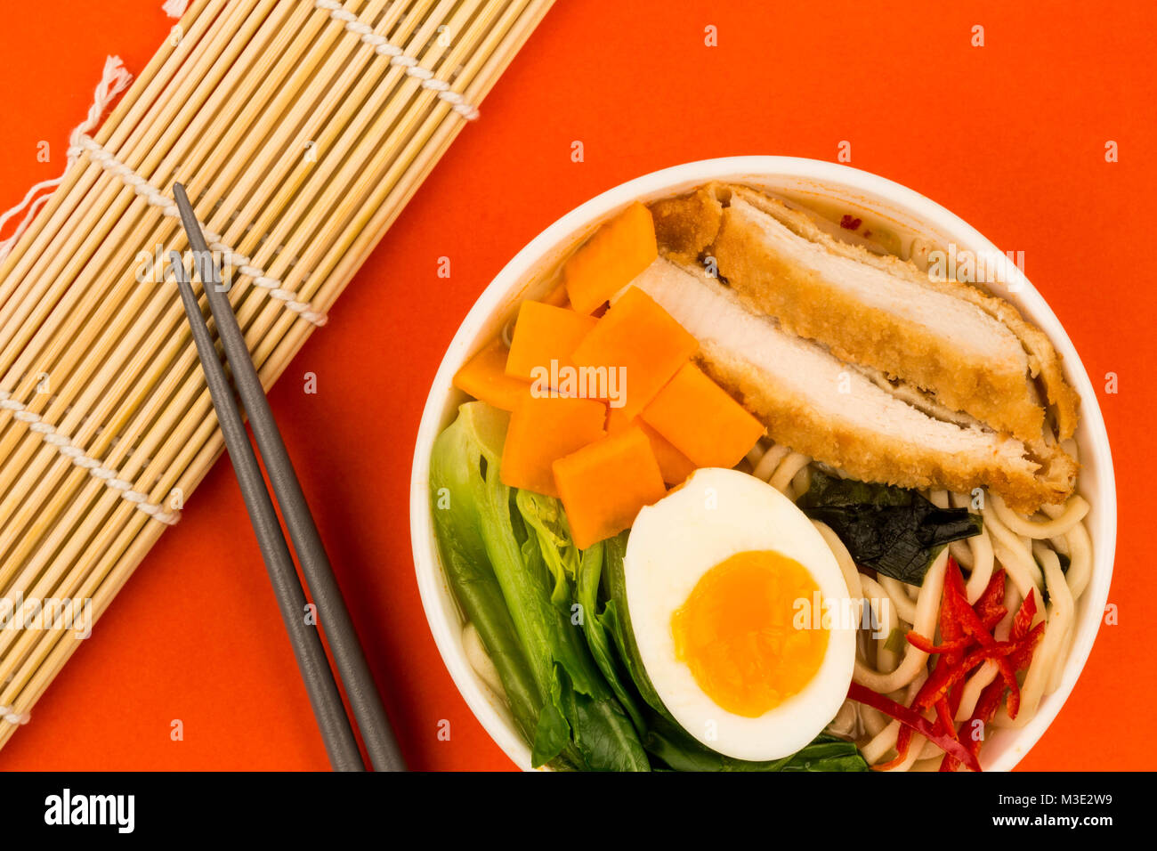 Japanese Style Panko Breadcrumbs Chicken And Noodle Broth or Soup With Sweet Potatoes Against A Red Background Stock Photo