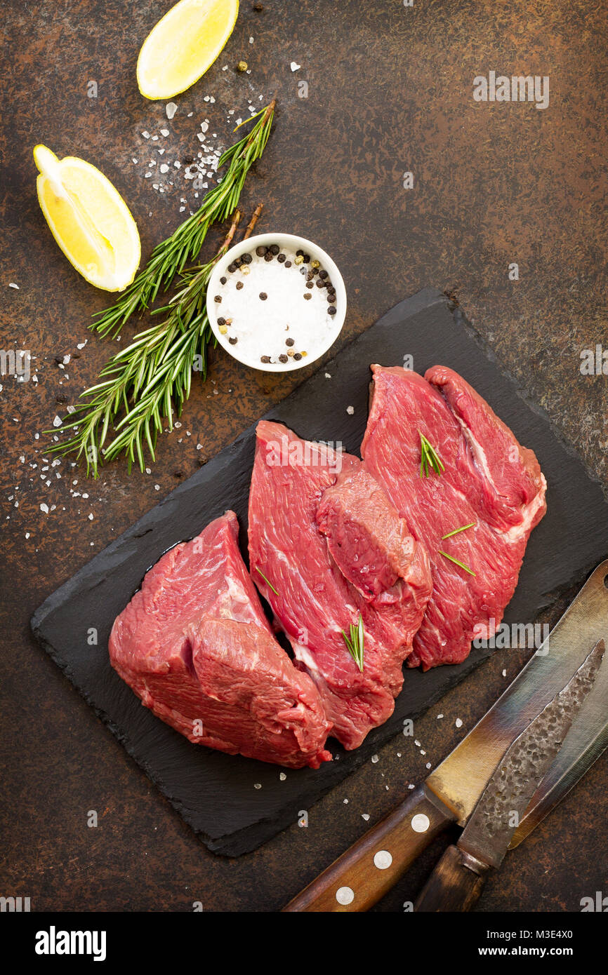 Fresh meat. Cheese steak beef on a slate cutting board, lemon, spices and fresh rosemary on a stone table. Stock Photo