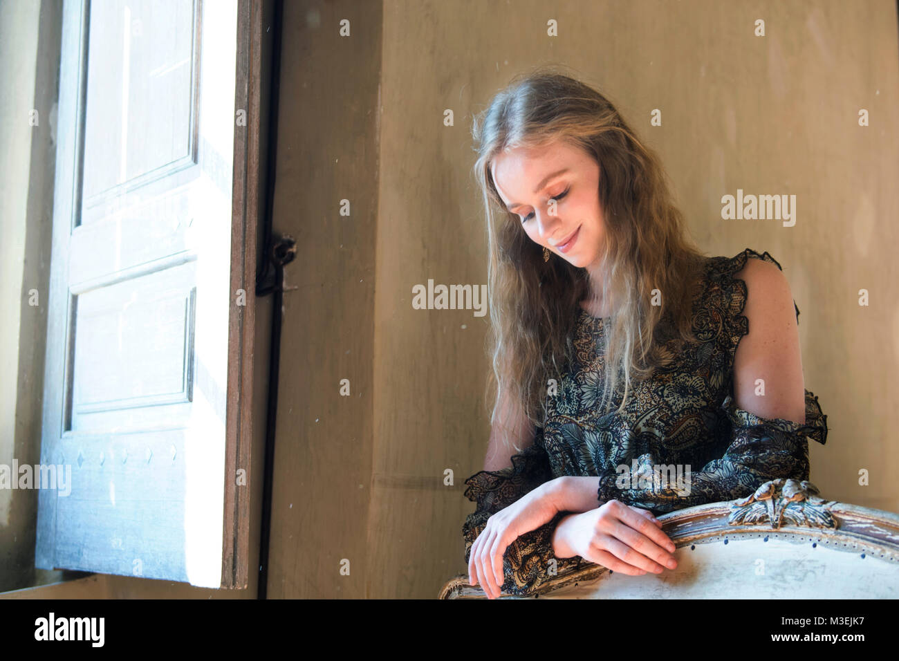 Beautiful young woman leaning over a settee by a window. Stock Photo