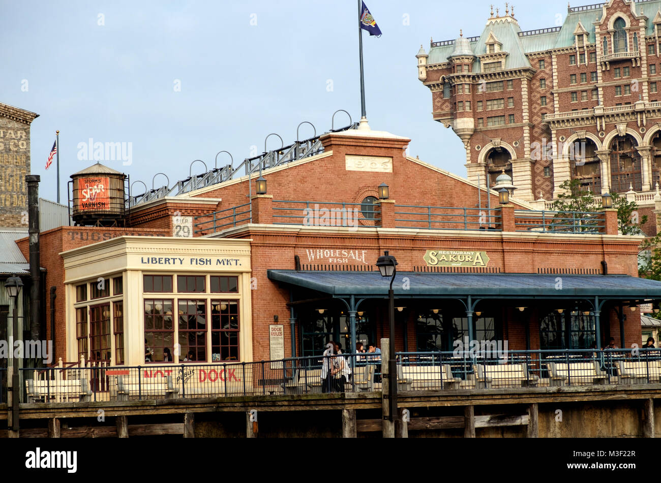 Vintage American building on a pier with large awning and benches in front. Back right is tall building. Old water tower on roof back left. Disneysea. Stock Photo