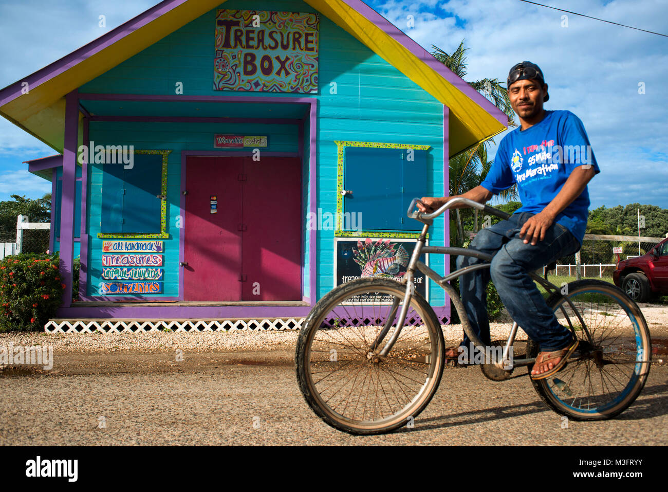 Local man in a bicycle next to a souvenir shop in Placencia village, Belize Stock Photo