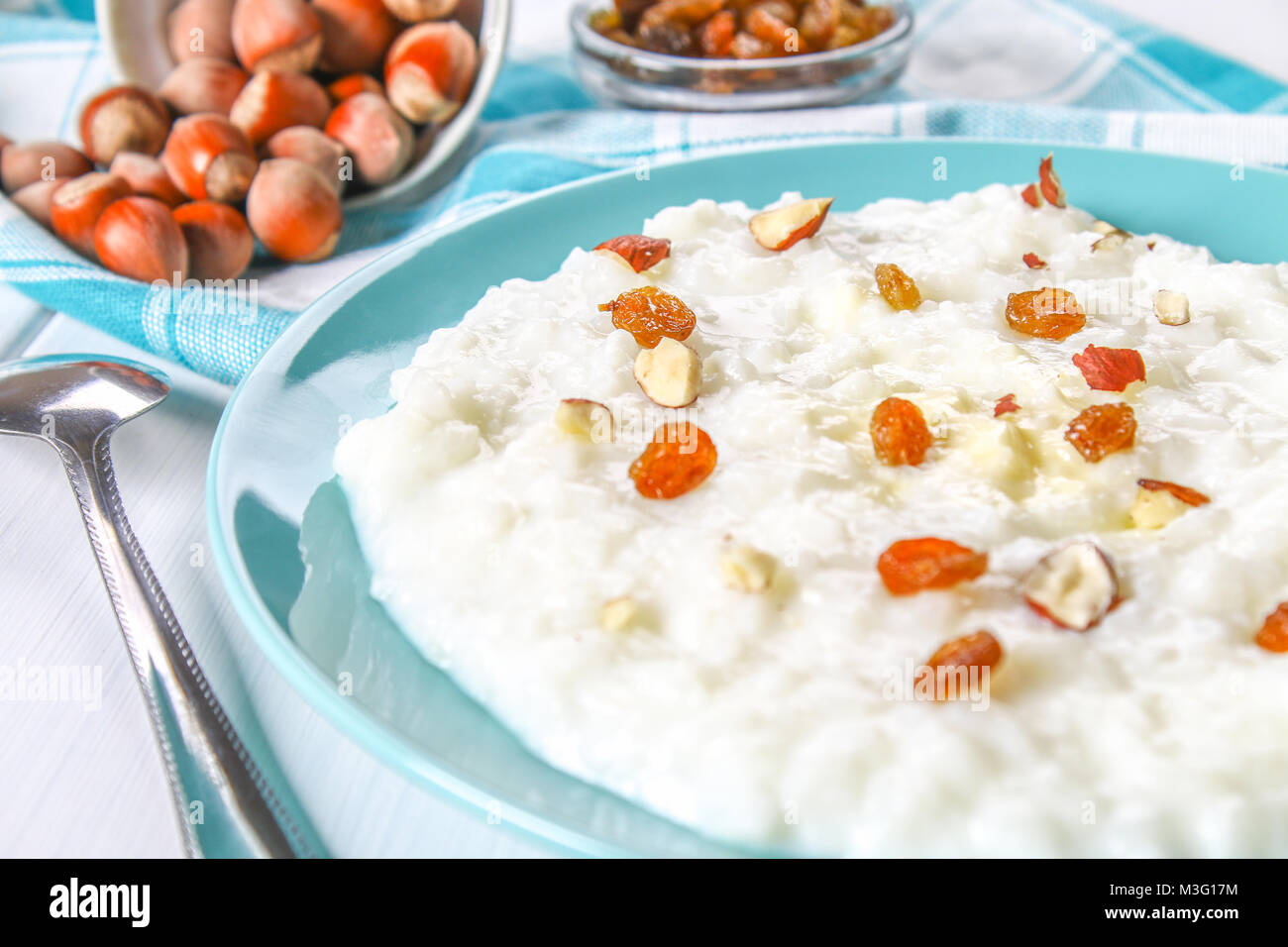 Rice milk porridge with nuts and raisins in a blue dish on a white wooden table Stock Photo