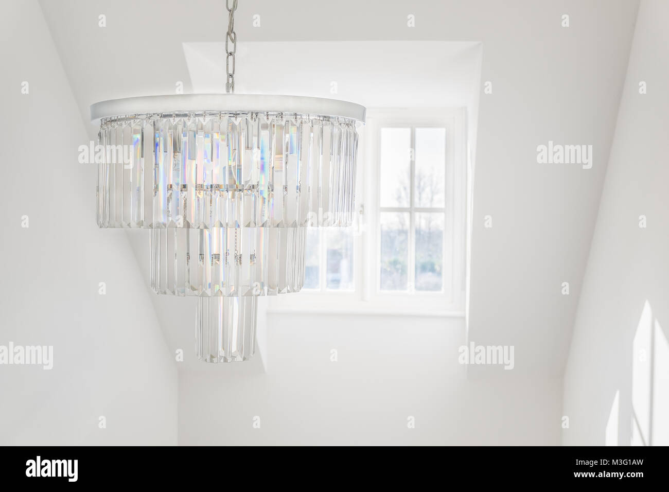 glass chandelier hanging infront of a dormer window in a bright white room Stock Photo